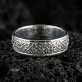 Load image into Gallery viewer, Polished silver Celtic knot band ring on volcanic stone, crisp macro product photo emphasizing clean reflective edges and sharp engraving depth.