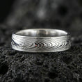 Load image into Gallery viewer, Polished silver Damascus-style band ring on volcanic stone, clean macro product photo emphasizing crisp woodgrain flow and reflective silver tones.