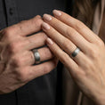 Load image into Gallery viewer, Oxidized Damascus-style band ring worn on a man and woman's finger, lifestyle wear photo showing strong contrast between darkened grooves and raised grain lines.
