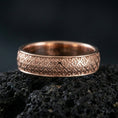 Load image into Gallery viewer, Rose gold plated fleur-de-lis band ring on volcanic stone, refined macro shot featuring soft rose highlights and sharp ornamental details.