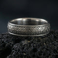 Load image into Gallery viewer, Oxidized sterling silver fleur-de-lis band ring on volcanic stone, macro close-up highlighting the repeating medieval motif and dark patina depth.