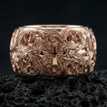 Load image into Gallery viewer, Rose gold plated ornate cross band ring on volcanic stone, refined macro shot capturing soft rose highlights on the cross centerpiece and ornate scroll detailing.