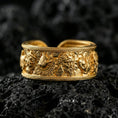 Load image into Gallery viewer, Gold plated mythic faces cuff band ring on volcanic stone, premium close-up showcasing warm gold tone across the raised portraits and textured background.
