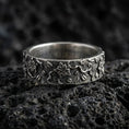 Load image into Gallery viewer, Oxidized sterling silver floral engraved band ring on volcanic stone, macro close-up highlighting raised blossoms, leaf motifs, and deep contrast texture.