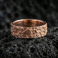Load image into Gallery viewer, Rose gold plated floral engraved band ring on volcanic stone, elegant macro shot capturing soft rose reflections, raised petals, and refined engraved depth.
