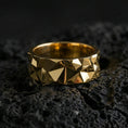 Load image into Gallery viewer, Gold plated faceted geometric band ring on volcanic stone, luxury macro photo showcasing warm gold tone across the pyramid facets and sculpted edges.