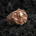 Load image into Gallery viewer, Rose gold plated skull signet ring with Celtic knot engraving on textured volcanic rock, luxury close-up capturing warm tone and sculpted skull depth