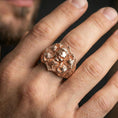 Load image into Gallery viewer, Rose gold plated skull signet ring worn on finger, close-up lifestyle photo showcasing the sculpted skull face and warm metallic glow