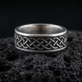 Load image into Gallery viewer, Sterling silver Celtic knot band ring on black volcanic stone, photographed with an oxidized patina that darkens the recessed background and sharpens the raised knotwork.