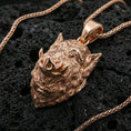 Load image into Gallery viewer, Rose gold plated boar head pendant on textured volcanic rock with braided chain, luxury close-up capturing warm tone and high-relief boar carving
