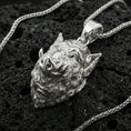 Load image into Gallery viewer, Polished silver boar head pendant on porous volcanic stone with braided chain, close-up highlighting sharp tusks and crisp sculpted details