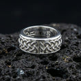Load image into Gallery viewer, Celtic knot spinner band ring on black volcanic stone, shown in a polished silver finish with crisp reflective edges across the raised knotwork.