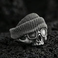 Load image into Gallery viewer, Oxidized sterling silver skull ring with beanie and goggles on black volcanic rock, macro close-up showing deep patina and streetwear texture
