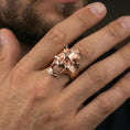 Load image into Gallery viewer, Rose gold plated open skull ring on a finger, close-up lifestyle photo showcasing warm plating tone, skull cutout shape, and detailed texture