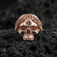 Load image into Gallery viewer, Rose gold plated gothic skull ring with laurel wreath on textured volcanic rock, luxury close-up capturing warm tone, carved leaf crown and vintage-style patina depth