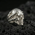 Load image into Gallery viewer, Polished silver skull ring with claw hand details on porous volcanic stone, close-up highlighting crisp teeth lines, smooth dome skull and sculpted finger bones