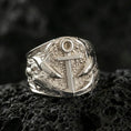 Load image into Gallery viewer, Polished silver nautical anchor ring featuring raised sea-life textures and layered relief, close-up studio shot on porous volcanic stone