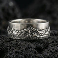 Load image into Gallery viewer, Oxidized sterling silver mountain landscape band ring on dark volcanic rock, rugged alpine relief texture, premium macro product shot.