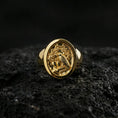 Load image into Gallery viewer, Gold plated raven crest signet ring with detailed bird engraving and decorative foliage, product-only macro image on black volcanic rock