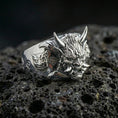 Load image into Gallery viewer, Polished silver Japanese Oni mask statement ring featuring raised horned demon head and carved swirl accents, close-up on volcanic stone