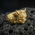 Load image into Gallery viewer, Gold plated Oni mask ring with sculpted horned demon face and engraved side emblem, product-only macro shot on black volcanic rock