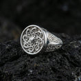 Load image into Gallery viewer, Polished silver round signet ring featuring raised spiral sun motif and engraved geometric band details, close-up on volcanic stone