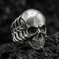 Load image into Gallery viewer, Oxidized sterling silver skull ring with smooth dome forehead and deep blackened eye sockets, macro product photo on black volcanic rock