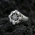 Load image into Gallery viewer, Polished silver compass signet ring featuring a dimensional navigation star and engraved direction letters, close-up on volcanic stone