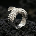 Load image into Gallery viewer, Polished silver adjustable wing ring featuring detailed feathers and a raptor head tip, close-up product shot on volcanic stone