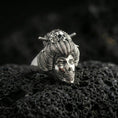 Load image into Gallery viewer, Polished silver Japanese geisha skull ring featuring sculpted facial detail, ribbed hair texture, and hairpin accents, close-up on volcanic stone