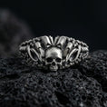 Load image into Gallery viewer, Oxidized sterling silver skull ring with crown-like spikes and chain-link band details, macro product photo on black volcanic rock
