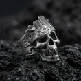 Load image into Gallery viewer, Oxidized sterling silver skull ring with carved woodgrain texture and engraved band details, macro product photo on black volcanic rock