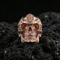 Load image into Gallery viewer, Rose gold plated cyber skull ring with futuristic mechanical engraving and high-contrast skull relief, close-up on volcanic rock