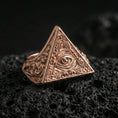 Load image into Gallery viewer, Rose gold plated pyramid triangle signet ring with all-seeing eye emblem and ornamental scrollwork, close-up on volcanic rock