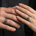 Load image into Gallery viewer, Oxidized sterling silver engraved ornament band worn on finger, faceted diamond panel detail, natural lifestyle hand shot with shallow depth of field.