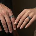 Load image into Gallery viewer, Oxidized sterling silver rope edge engraved band worn on finger, floral panel and scrollwork detail, natural lifestyle hand shot with shallow depth of field.