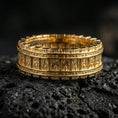 Load image into Gallery viewer, Gold plated railway track band ring on volcanic rock, detailed riveted borders with rugged mechanical texture, luxury jewelry product photography.