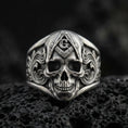 Load image into Gallery viewer, Oxidized sterling silver Masonic skull ring with compass-and-G emblem and engraved scrollwork, on black volcanic rock