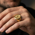 Load image into Gallery viewer, Gold plated Lucifer sigil signet ring worn on a finger, close-up lifestyle photo focusing on the raised emblem and contrast detailing
