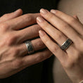 Load image into Gallery viewer, Oxidized sterling silver spinning wave band worn on finger of a man and a woman, nautical swirl engraving detail on rotating center, natural lifestyle hand shot with shallow depth of field.