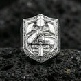 Load image into Gallery viewer, Sterling silver knight signet ring in a polished silver finish, raised medieval warrior and sword relief on a shield face, close-up on volcanic stone