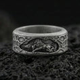 Load image into Gallery viewer, Oxidized sterling silver spinning lion band ring on dark volcanic rock, engraved lion scene on rotating center with textured border, premium macro product shot.