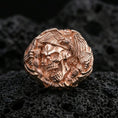 Load image into Gallery viewer, Sterling silver skull ring with a rose gold plated finish, detailed skull and eagle motif with sculpted wings, close-up on volcanic rock