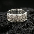 Load image into Gallery viewer, Polished silver engraved ornament band ring on black volcanic stone, crisp floral medallion panel with detailed scrollwork borders, centered close-up studio lighting.