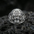 Load image into Gallery viewer, Sterling silver masonic skull ring in a polished silver finish, detailed skull face with ornate side engravings and pyramid eye symbol, close-up on volcanic stone