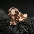 Load image into Gallery viewer, Sterling silver shattered skull ring with a rose gold plated finish, gothic skull statement ring with fractured silhouette and textured finish, close-up on volcanic rock