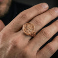 Load image into Gallery viewer, Sterling silver heraldic phoenix ring on a finger, macro lifestyle shot featuring the rose gold plated finish and intricate engraved emblem details