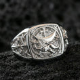 Load image into Gallery viewer, Sterling silver heraldic lion ring in a polished silver finish, bold signet design with raised lion emblem, cross motif, and engraved side symbols, close-up on volcanic stone