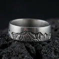 Load image into Gallery viewer, Oxidized sterling silver Grand Teton mountain band ring on dark volcanic rock, detailed alpine skyline engraving, premium macro product shot.