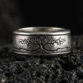 Load image into Gallery viewer, Oxidized sterling silver Yggdrasil spinner band ring on dark volcanic rock, engraved tree of life on rotating center with mountain line detail, premium macro product shot.